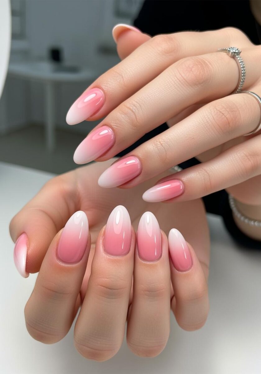 Two hands displaying pink ombre almond-shaped nails with white tips, one hand wearing a diamond ring