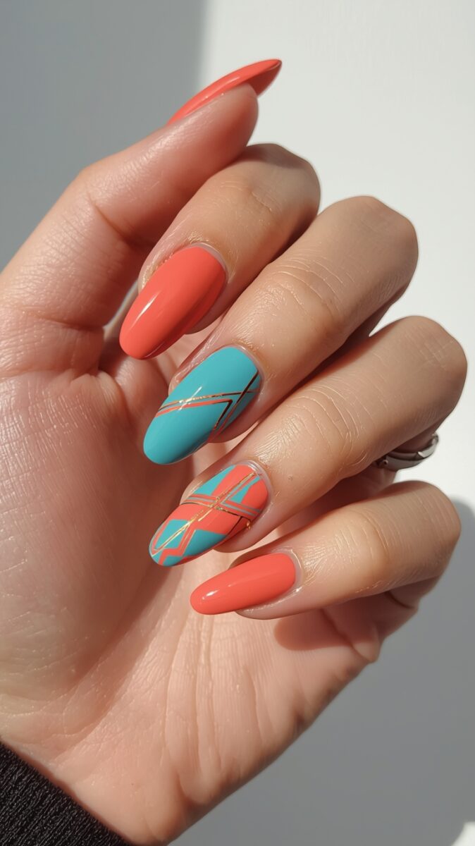 Hand with almond-shaped nails featuring coral orange polish and two accent nails in turquoise with gold geometric lines