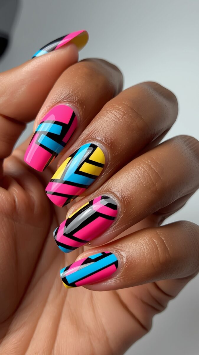 Hand with bold geometric nail art featuring neon pink, blue, yellow, and black patterns on square nails