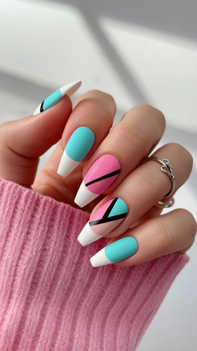 Hand with long coffin-shaped nails featuring geometric pink, teal, white, and black nail art design