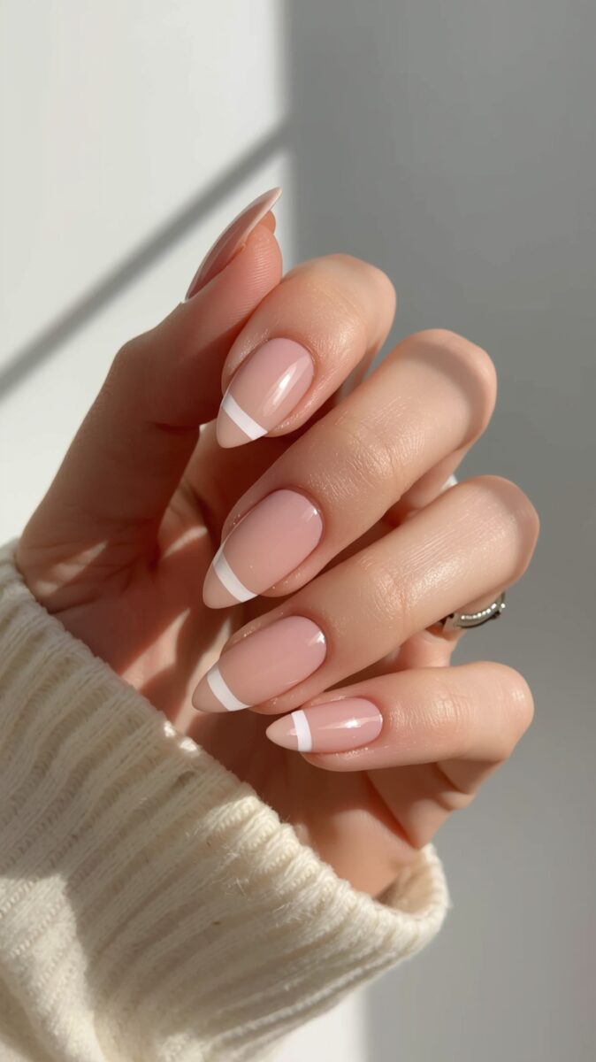 Close-up of a hand with almond-shaped French manicure nails featuring nude pink base and white tips