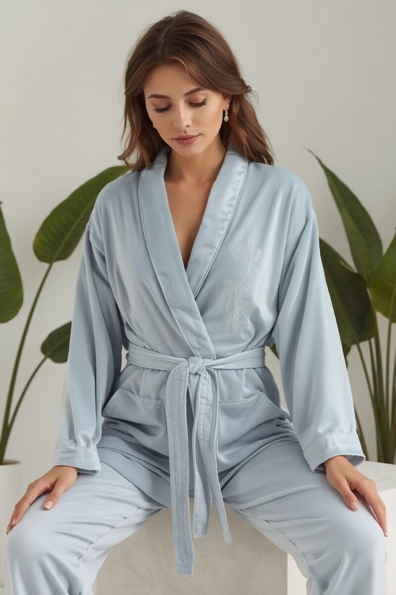 Woman wearing a light blue kimono-style robe with belt tie and floral embroidery, seated against a white background