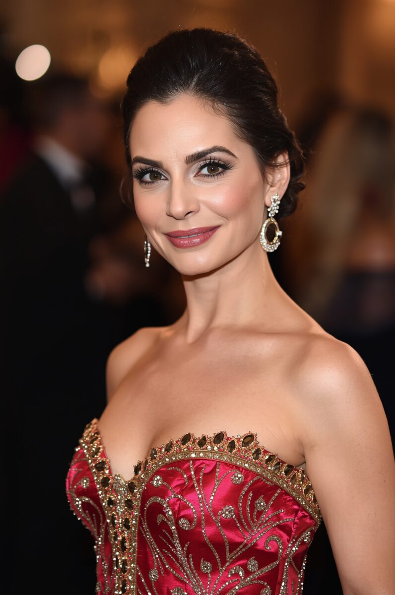 Elegant woman in red and gold embroidered strapless gown with diamond earrings at a formal event