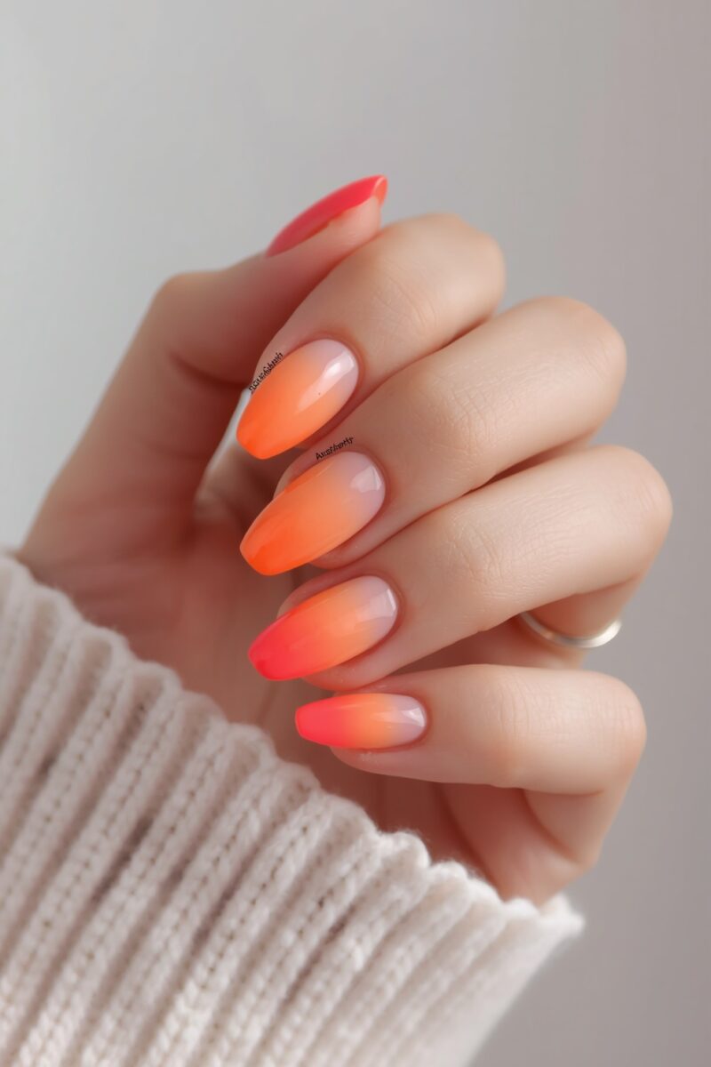 Hand with almond-shaped nails featuring orange to coral-red ombre gradient nail art on neutral background