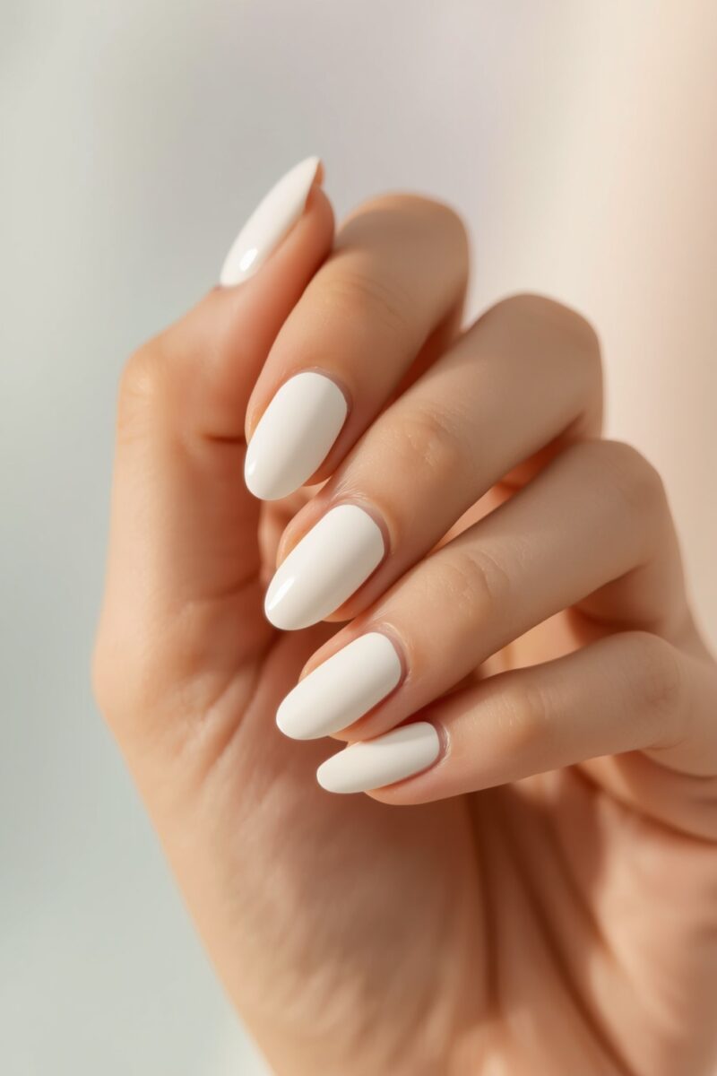 Close-up of a hand with perfectly manicured almond-shaped nails painted in glossy white nail polish