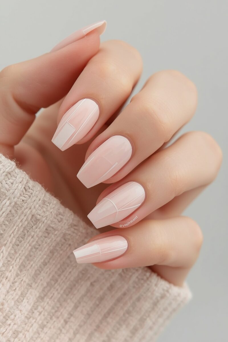 Close-up of hand with long coffin-shaped blush pink nails featuring subtle white geometric line nail art