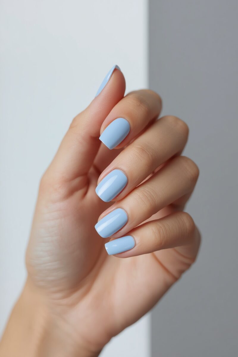 Close-up of a hand with glossy light blue square-shaped nail polish against a white background