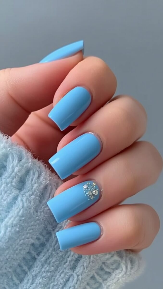 Hand with square-shaped baby blue acrylic nails, one ring finger nail adorned with rhinestone crystals