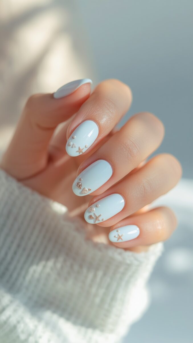 Hand with baby blue oval nails featuring tiny gold starfish and heart nail art embellishments