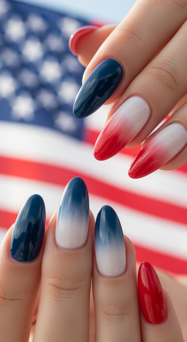 Hands with red, white, and blue ombre gradient nail art in front of blurred American flag