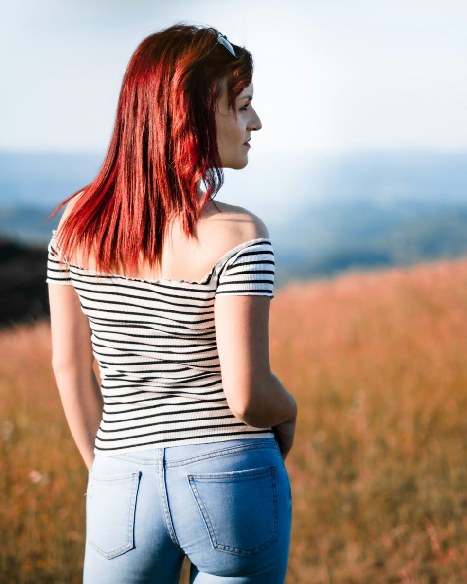 A fitted off-shoulder top with black stripes and plain light-wash jeans, seen from behind in a field of golden grass