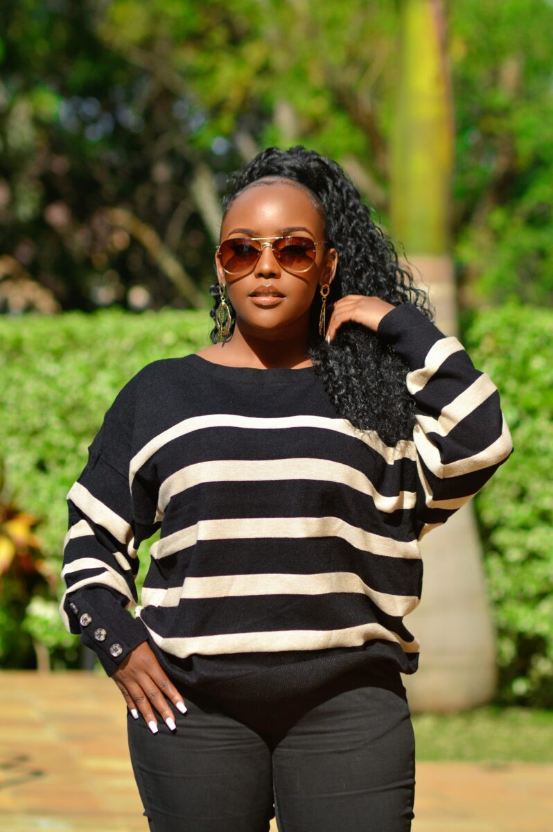 A black sweater with wide cream stripes and buttoned cuffs, worn with black pants, aviator sunglasses and big gold earrings