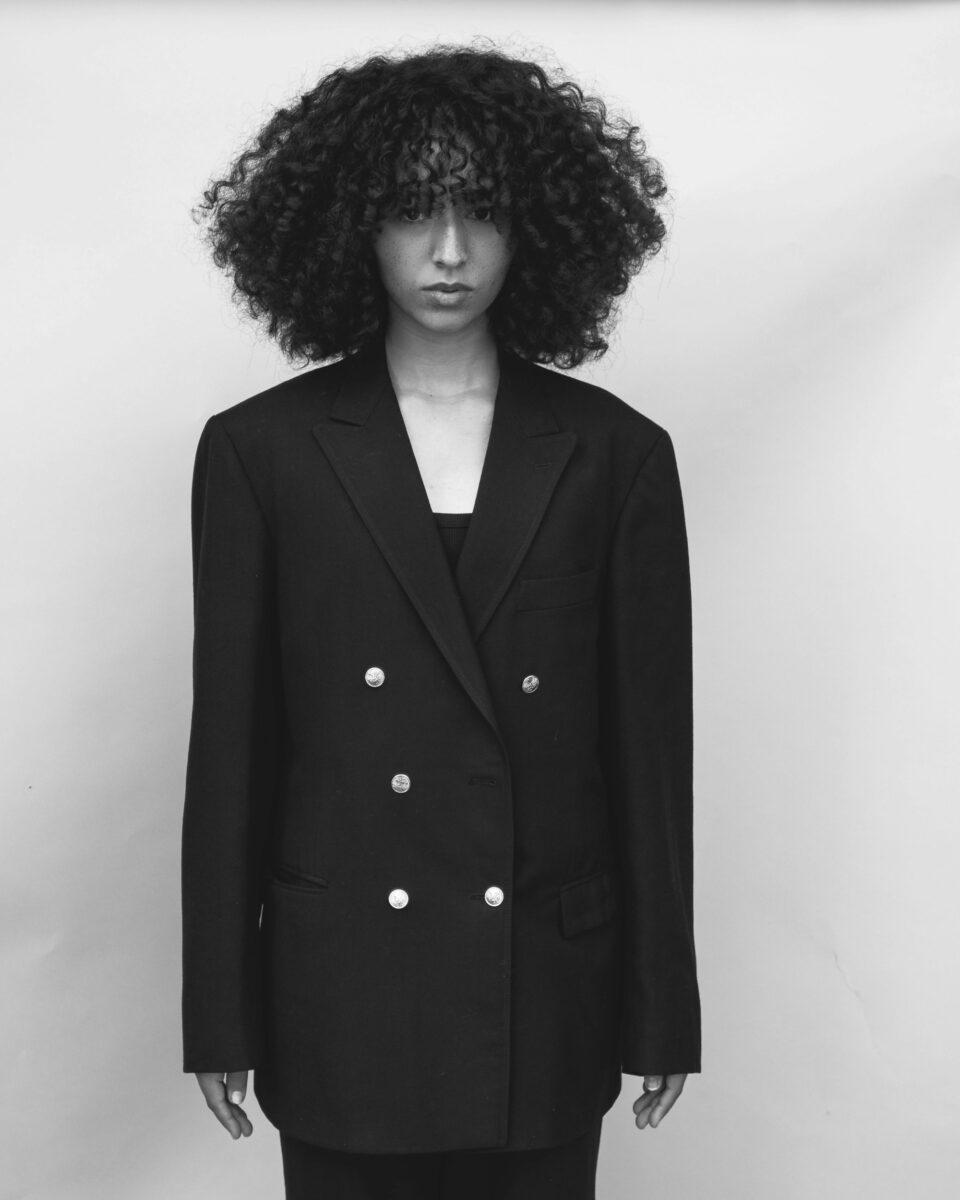 Black and white portrait of a woman in an oversized black double-breasted blazer with six metal buttons