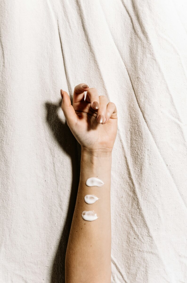 Three dabs of white cream on the inside of a woman's forearm on a linen backdrop