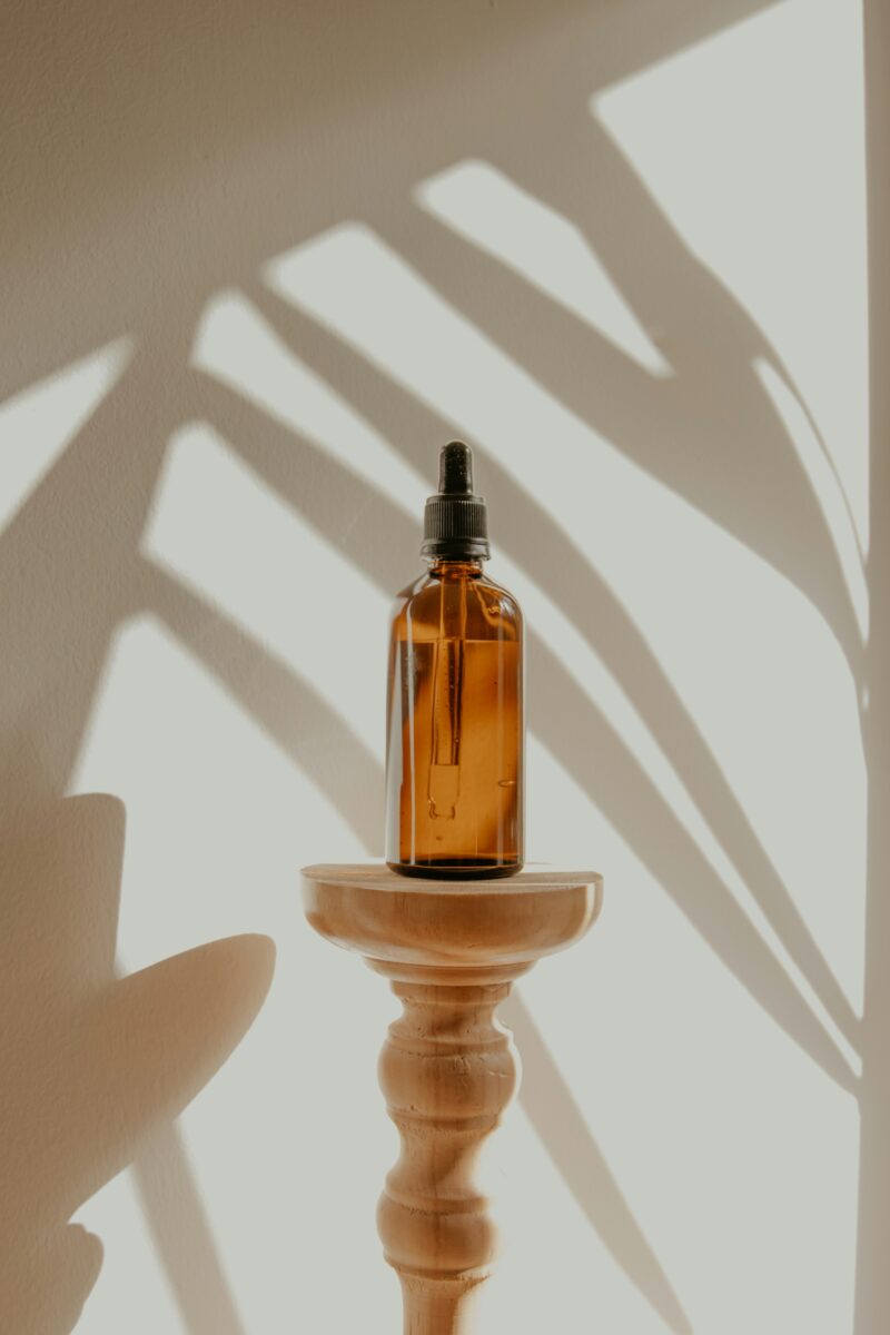 An amber glass serum bottle with a black dropper on a wooden stand