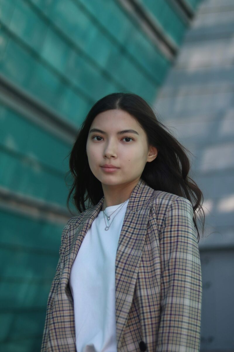 Woman in a brown check blazer over a white crew-neck T-shirt with two fine layered necklaces