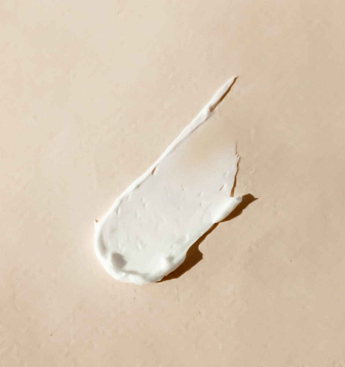 A thick smear of white face cream on a beige surface