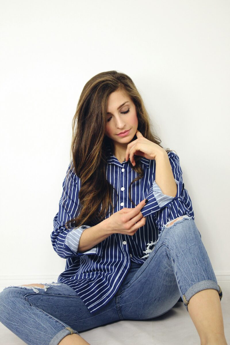 A navy shirt with white vertical stripes, sleeves rolled to show a lighter cuff, worn with ripped light-wash jeans cuffed at the ankle