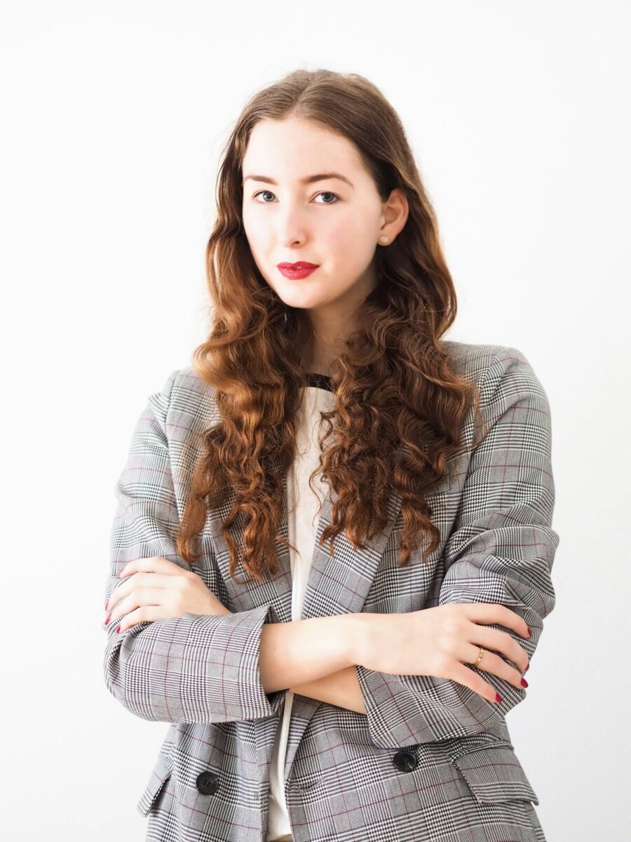 A gray check blazer over a white top, arms crossed, against a plain white wall
