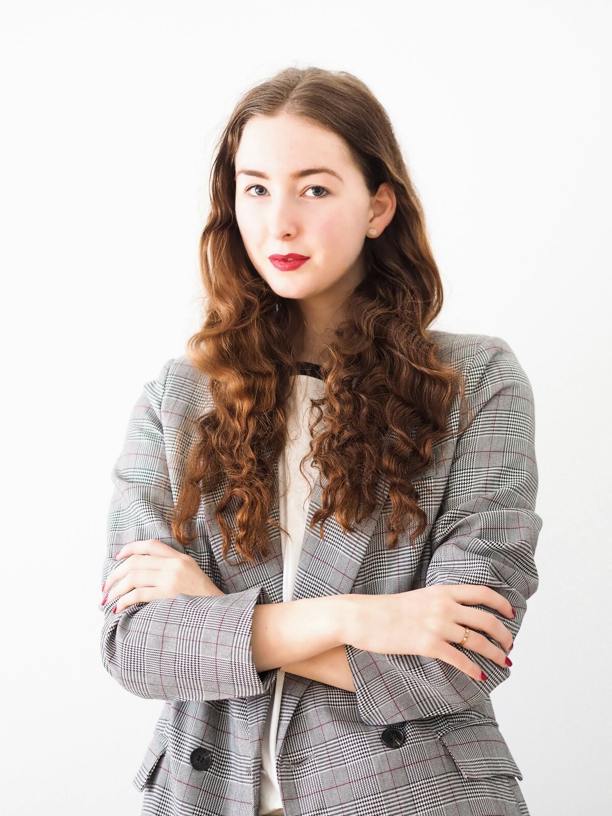 A gray check blazer over a white top, arms crossed, against a plain white wall