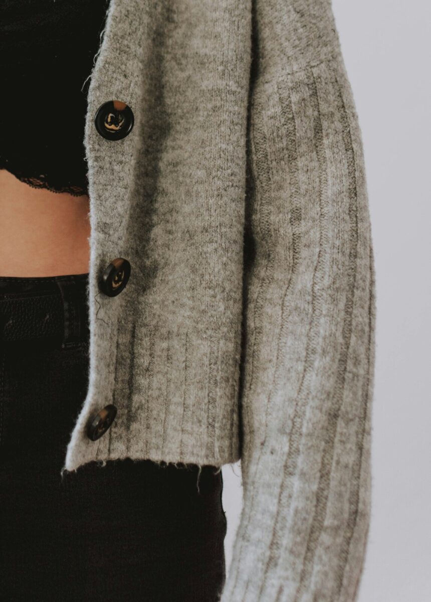 A gray ribbed cardigan with dark buttons, worn open over a black top