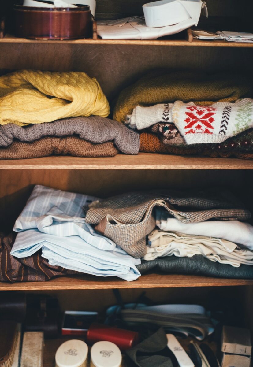 Folded sweaters, shirts and a tweed jacket on wooden closet shelves
