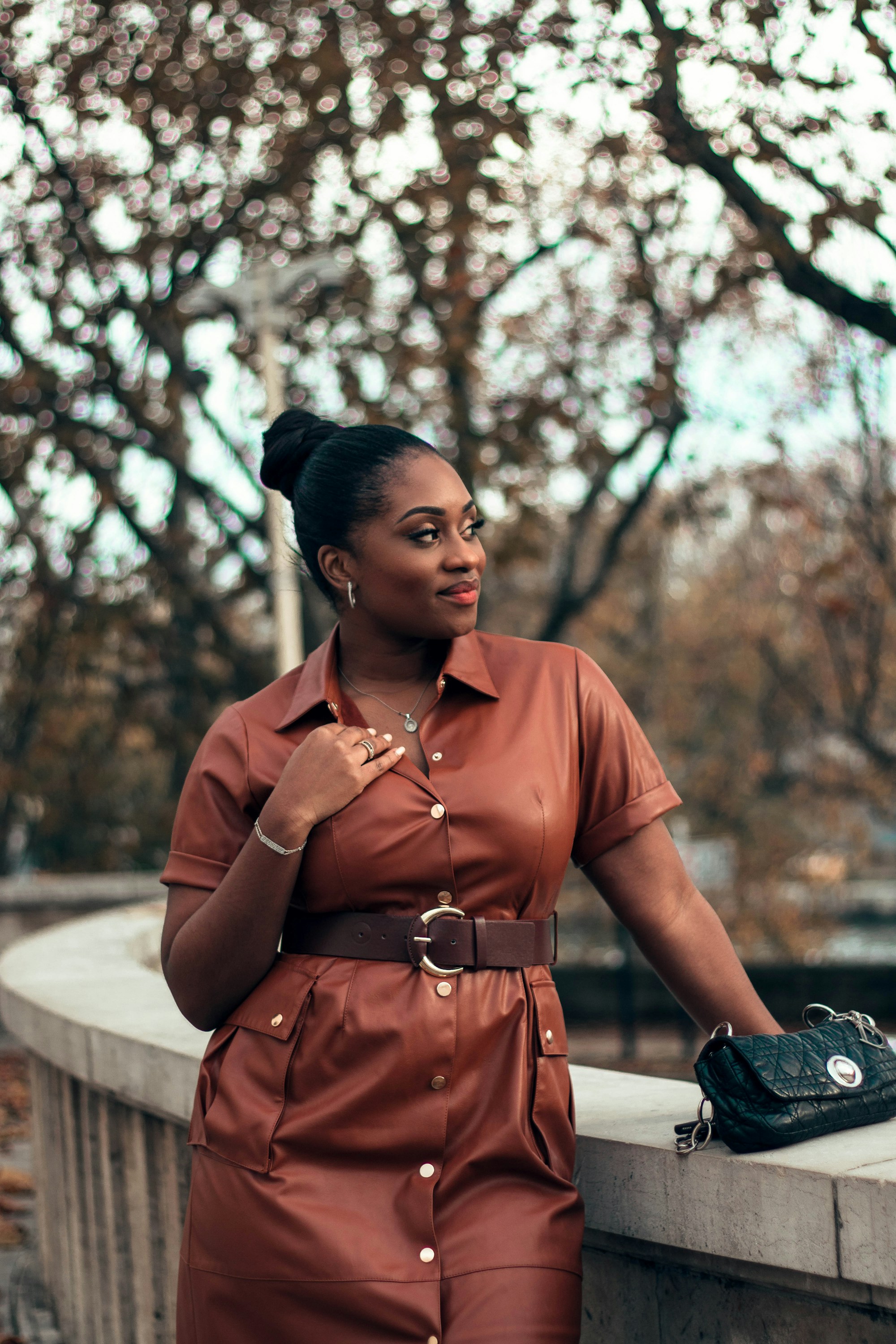 woman in a cognac leather-look shirt dress with a dark brown belt and a black quilted bag