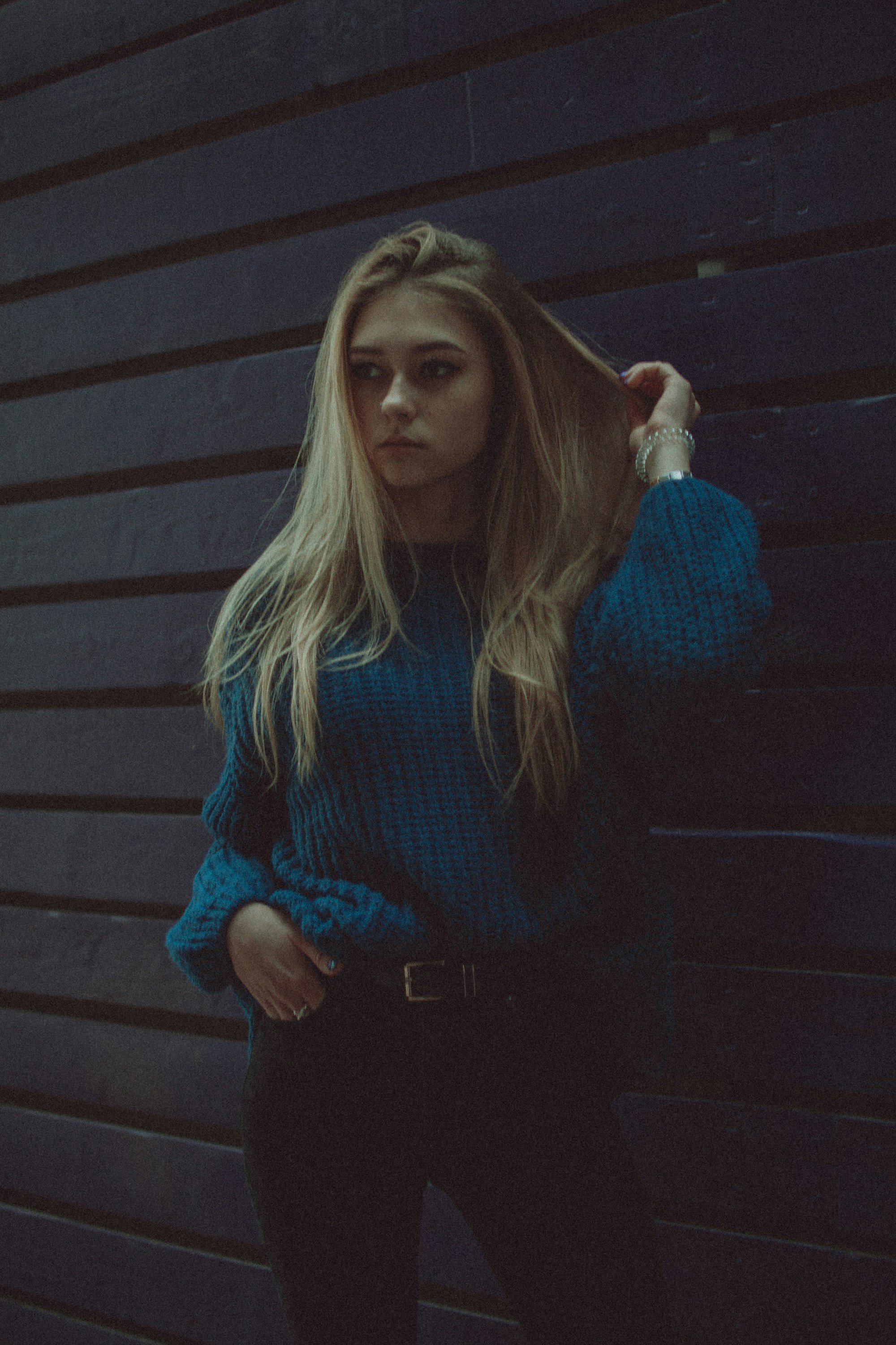 woman in a chunky teal knit sweater tucked into black pants with a black belt
