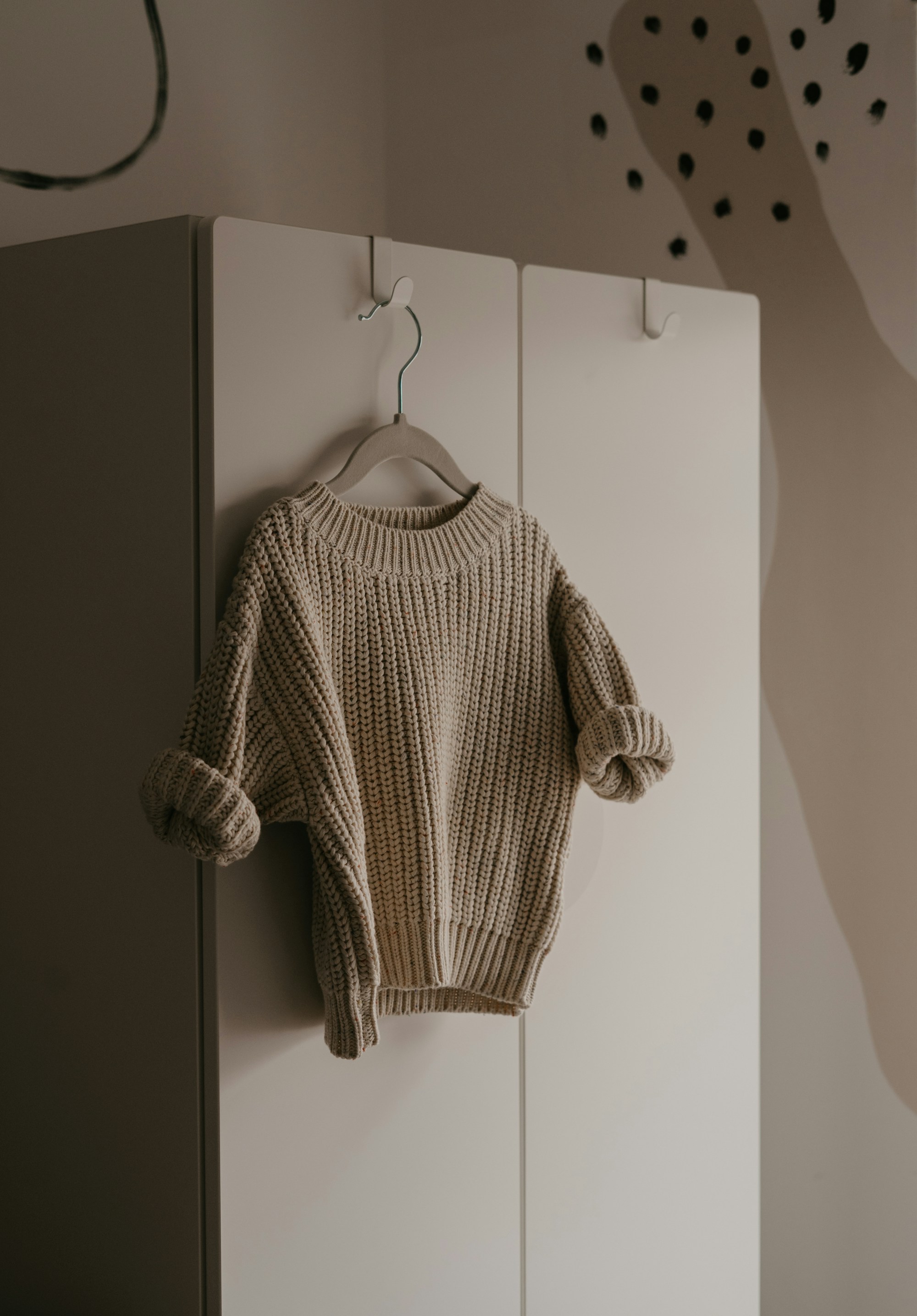 oatmeal chunky rib knit sweater on a hanger hooked over a white wardrobe door