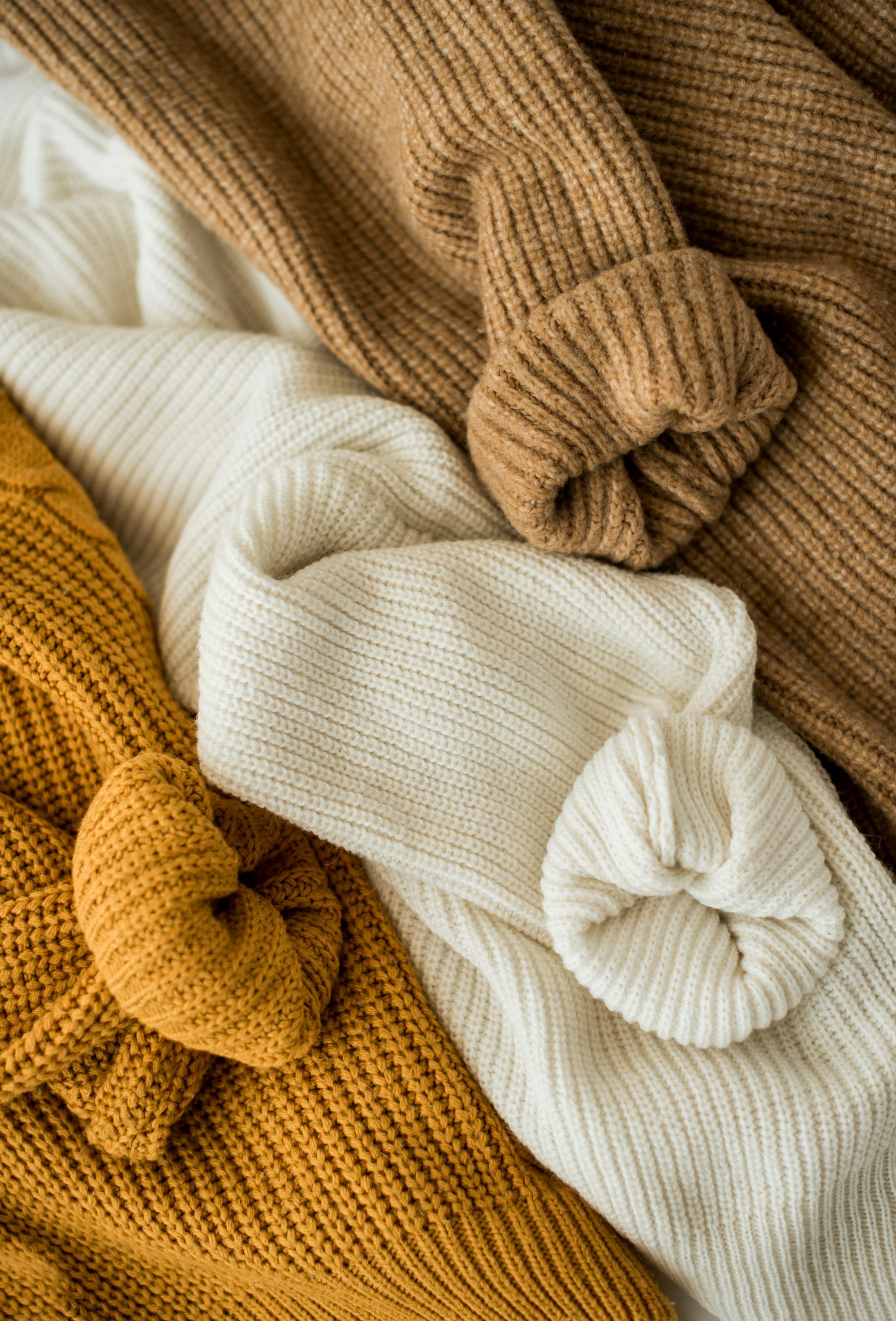 pile of mustard, cream and camel rib knit sweaters with rolled cuffs