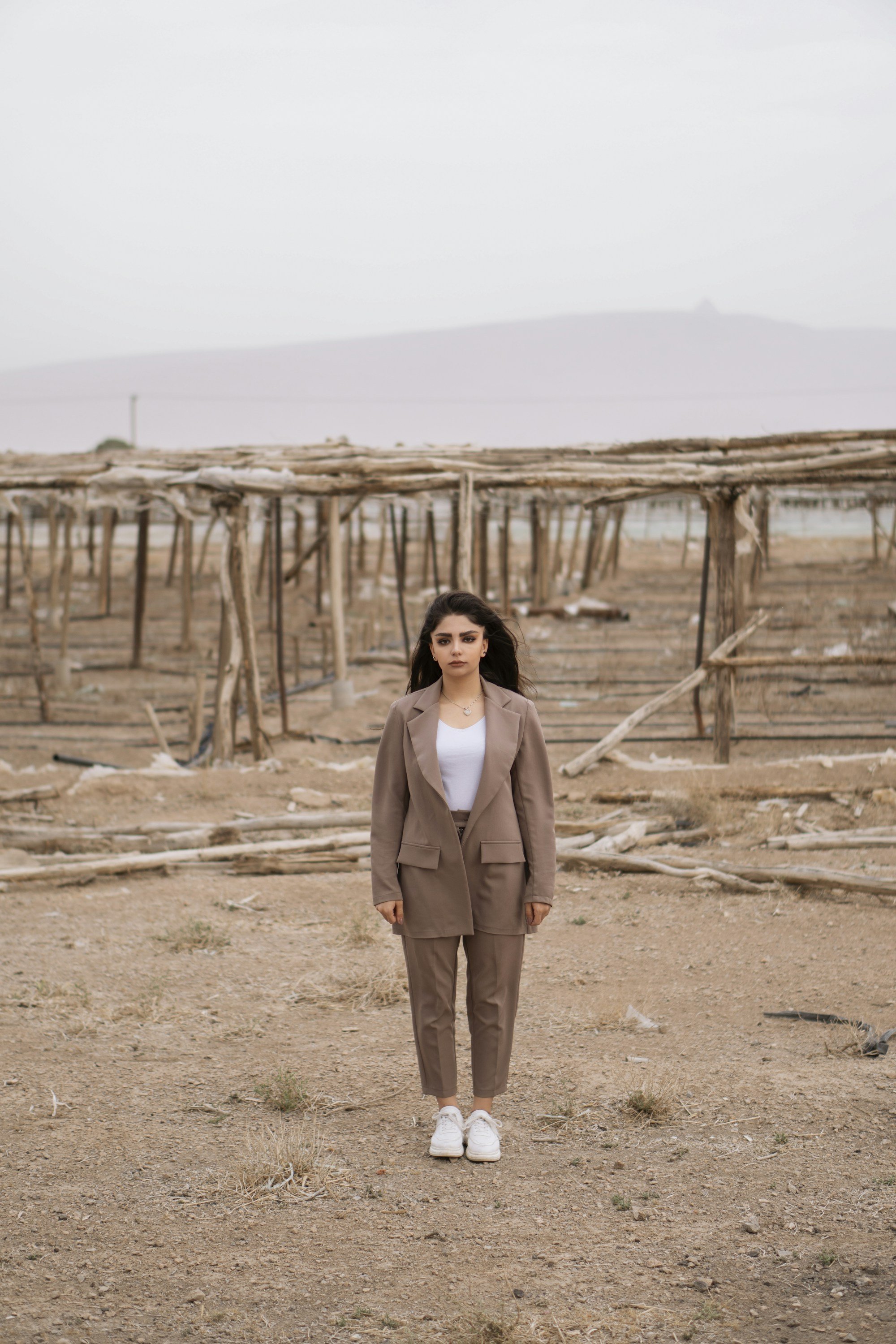 woman in a mocha suit, white top and white sneakers standing on dry ground